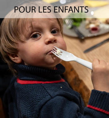 Un jeune enfant mange de la raclette en nous regardant, sa fourchette à la bouche